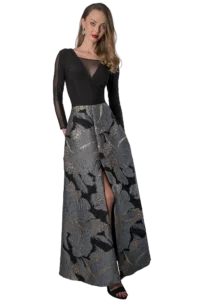 Woman in a black long-sleeve top with sheer panels and a metallic floral-print skirt, standing with one leg forward and red lipstick.