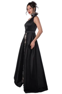 Woman in a black evening gown with a patterned scarf tied at the neck, standing in a side pose against a black background.