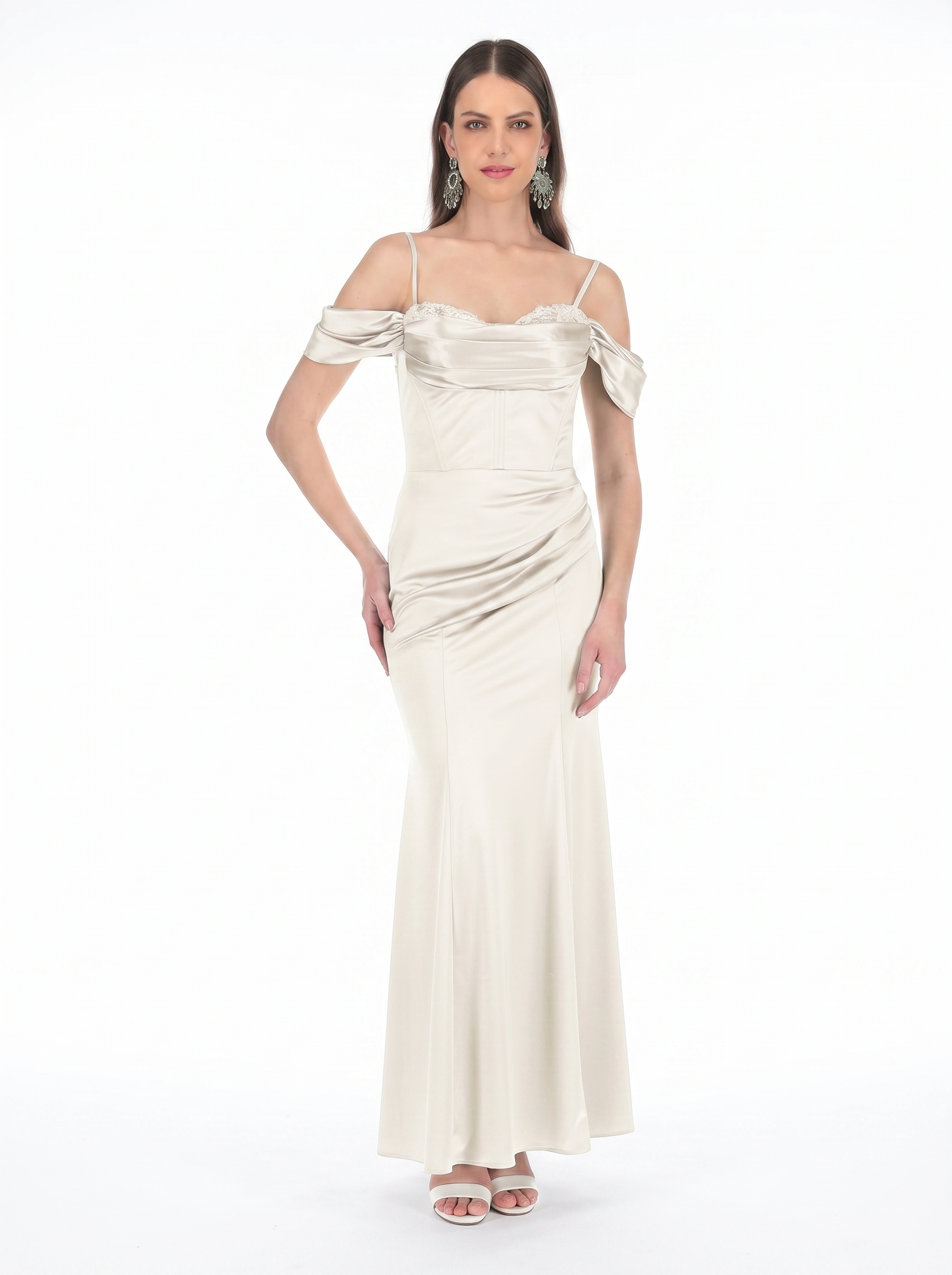 Woman in ivory satin off-shoulder evening gown with lace trim, posing with hand on hip and wearing large chandelier earrings.