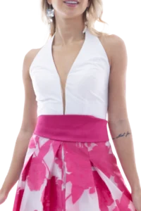 Woman wearing a white halter top and bright pink floral skirt, waist up, against a light background.