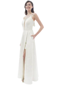 Smiling woman in a white lace evening gown with a deep V neckline and a front slit, hands in pockets.