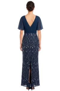 Back view of a woman in a navy evening gown with a V-shaped back, sheer flutter sleeves, and a lace-patterned skirt with a back slit