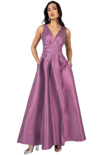 Full-length view of a woman in a mauve satin evening gown with a plunging V-neck and pockets, posing with hands in pockets.
