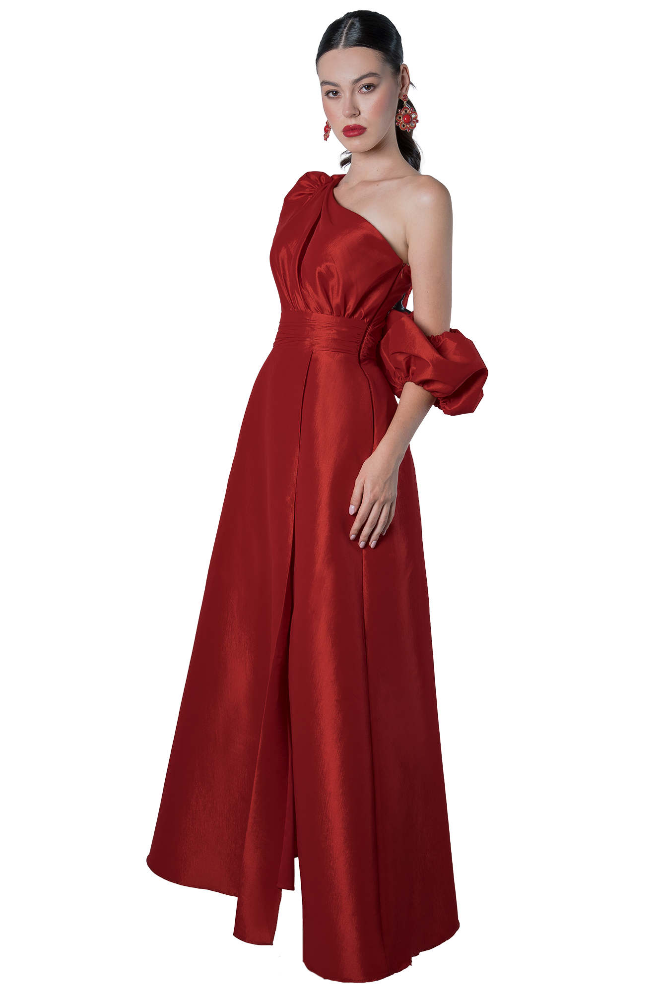 Woman in a floor-length red satin gown with one shoulder and a ruffled puff sleeve, standing against a black background wearing red lipstick and statement earrings.