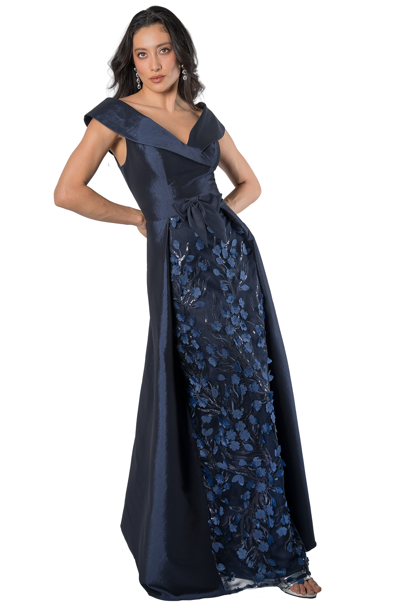 Woman in a navy blue off-the-shoulder gown with floral embroidery, standing with hands on hips and earrings visible.
