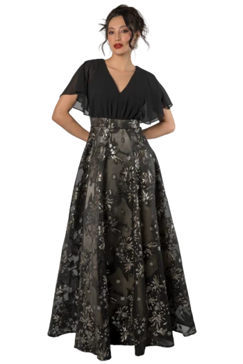 Woman in a black V-neck sheer blouse with a long floral lace skirt, posing with hands on hips.