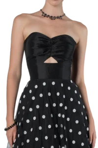 Woman in a black strapless dress with a small chest cutout and a white polka-dot skirt, wearing a beaded necklace.