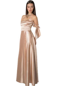 Woman in a champagne satin off-shoulder gown with bow sleeves and a statement necklace, posing confidently.