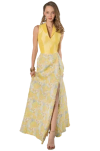 Woman in a bright yellow sleeveless blouse and a long pastel floral skirt with a side slit, posing confidently with jewelry.