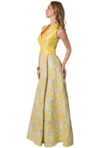 Side profile of a woman wearing a yellow sleeveless top and a long pastel floral skirt against a black background.