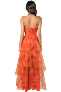 Back view of a woman wearing an orange floral strapless gown with a red beaded necklace, standing against a plain background.