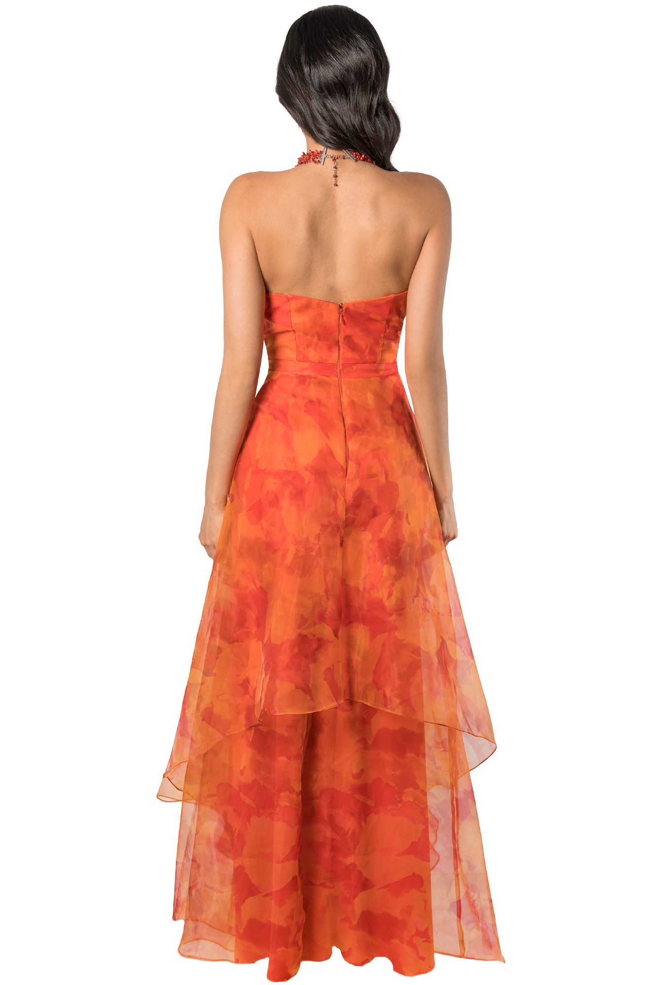 Back view of a woman wearing an orange floral strapless gown with a red beaded necklace, standing against a plain background.
