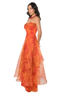 Woman in a bright orange, strapless evening gown with a red beaded necklace, posing in profile.