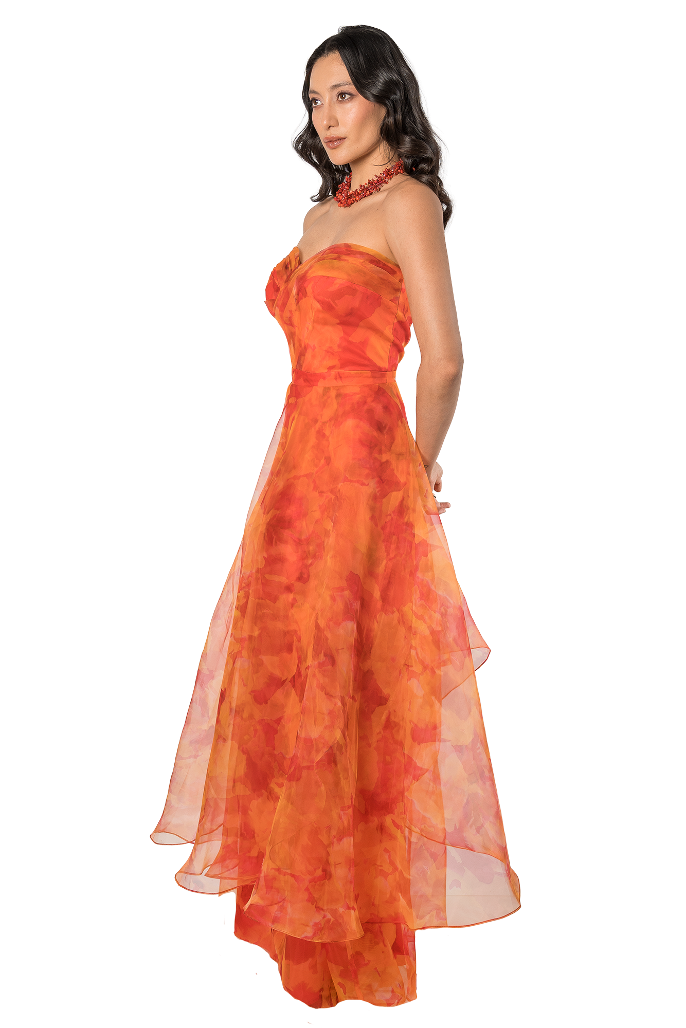 Woman in a bright orange, strapless evening gown with a red beaded necklace, posing in profile.