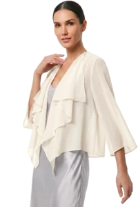 Woman wearing a light cream, ruffled cape over a silver gown, posing with hand near her neck.