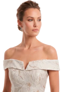 Portrait of a woman with an updo hairstyle, wearing a cream off-shoulder embroidered dress and dangling earrings, looking to the side.