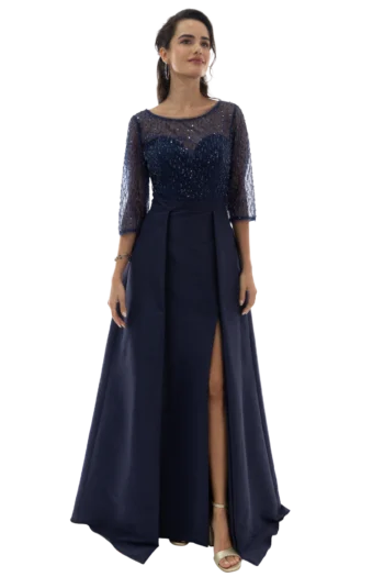 Woman in a navy sequined evening gown with sheer sleeves, standing with a slit showing her legs and sandals.