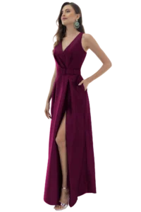 Woman in a magenta sleeveless gown with a high leg slit and matching belt, posing with one hand on hip and green statement earrings