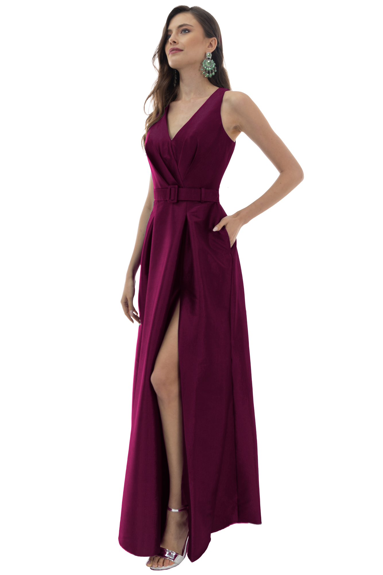 Woman in a magenta sleeveless gown with a high leg slit and matching belt, posing with one hand on hip and green statement earrings