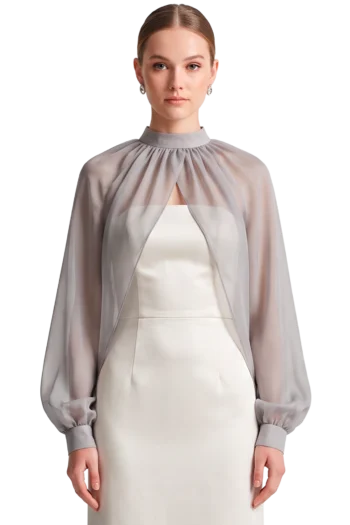 Portrait of a woman in a pale gray sheer cape over a white sheath dress, looking straight ahead.