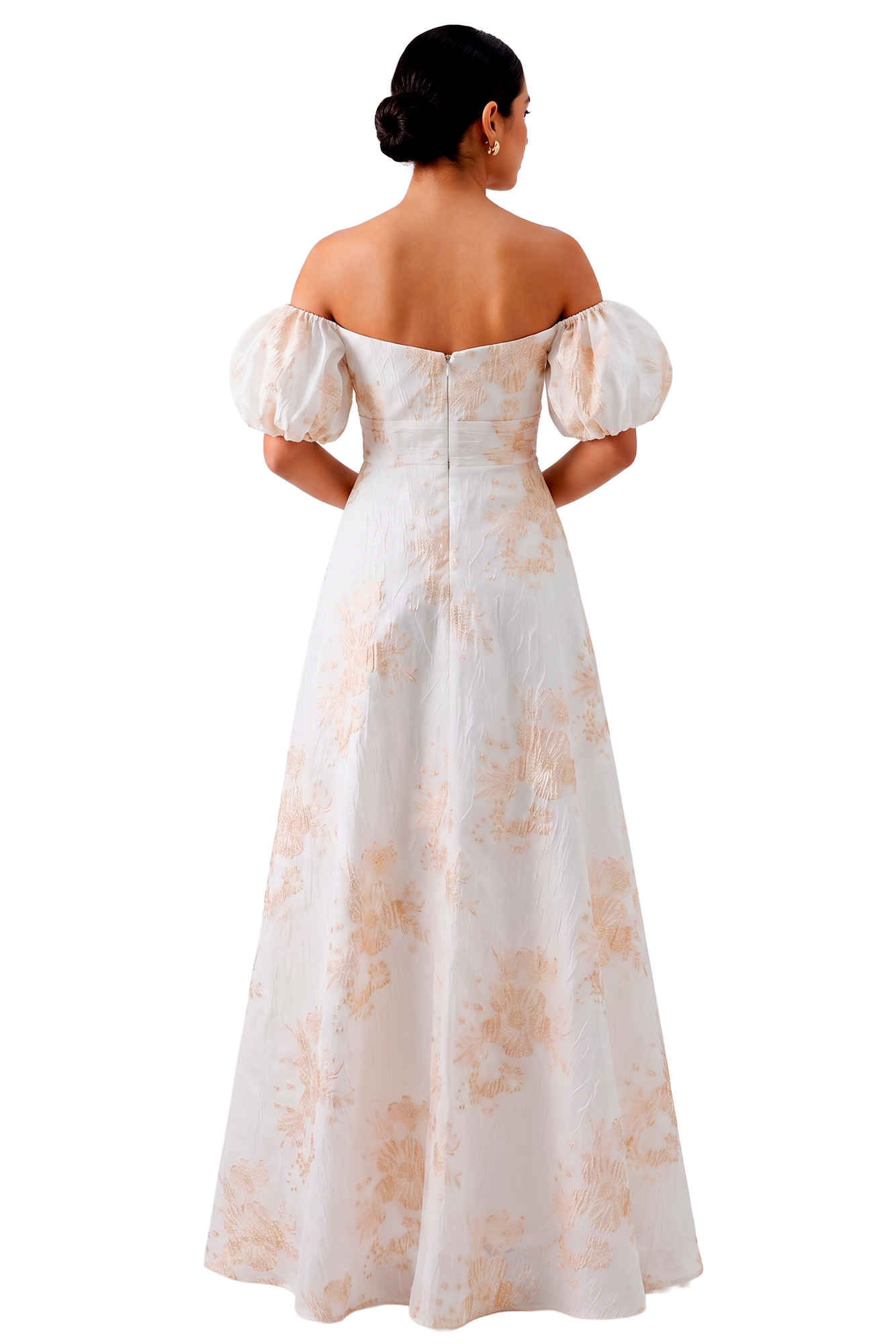 Back view of a woman in an off-the-shoulder white gown with peach floral pattern and a low bun, against a black background.