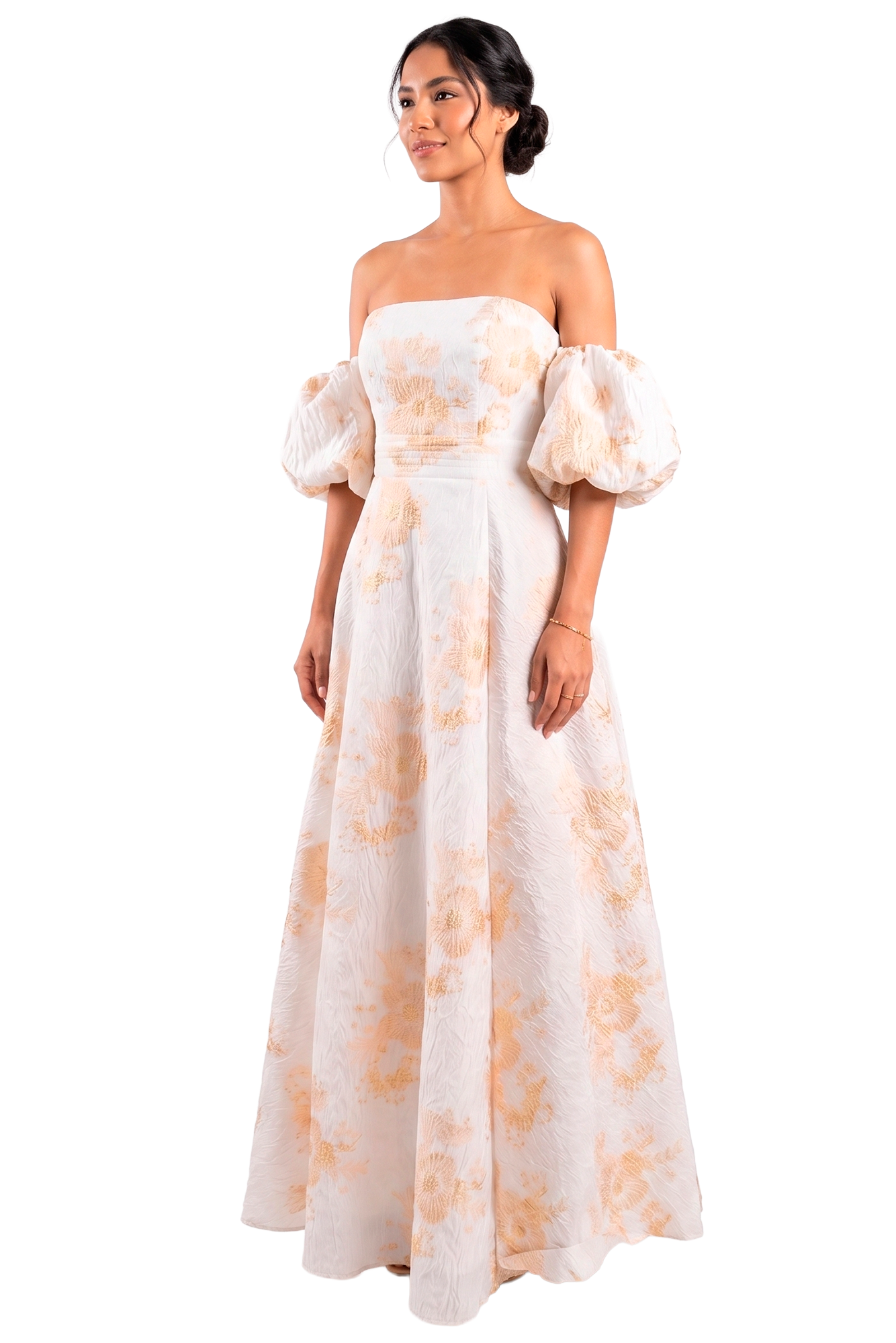 Woman in a strapless, floor-length white gown with peach floral print and puff sleeves, standing against a black background.