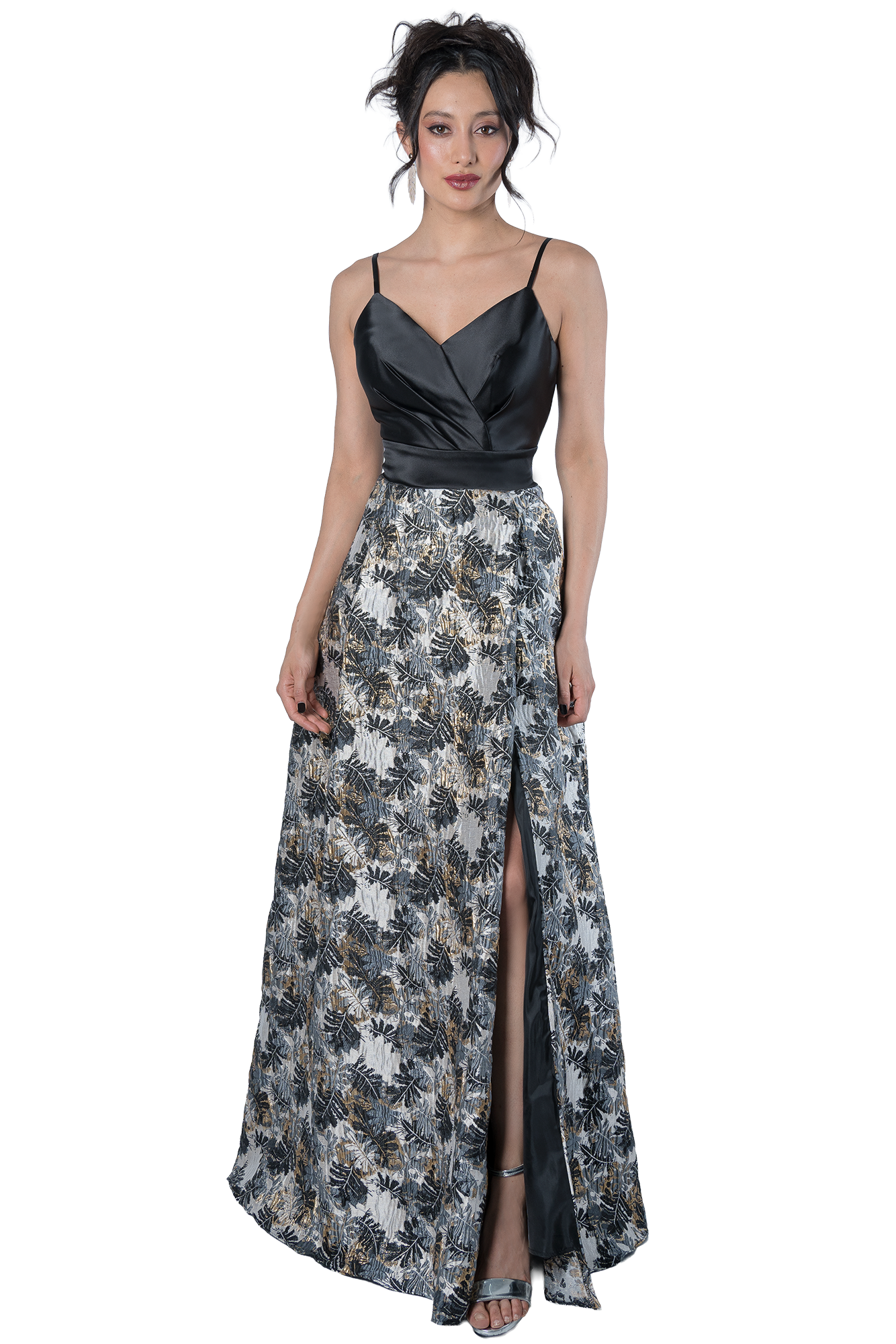 Woman in a black satin sleeveless top and a patterned, high-slit skirt posing against a black background.