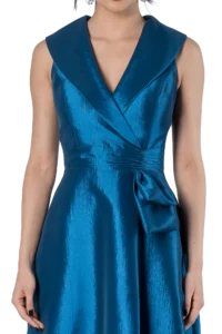 Woman wearing a sleeveless, metallic blue wrap dress with a deep V neckline and tied waist.