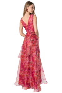 Woman in a pink floral evening gown photographed from behind, showing a V-back and flowing skirt, with red earrings visible on her left ear.