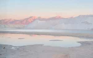 Snowy desert at sunrise with pink-tinted mountains and calm reflective pools in the foreground.