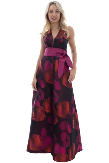 Mujer luciendo un elegante vestido de gala estampado con motivos florales fucsias, escote en V profundo con transparencia, lazo a la cintura y falda larga de jacquard con abertura frontal.
