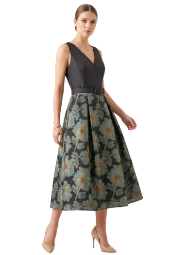 Mujer vistiendo un vestido de fiesta midi línea A con corpiño negro de escote en V, cinturón a juego y falda de jacquard estampada con tablones.